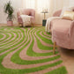 Living room with a green and brown patterned rug, pink sofa, and plant.